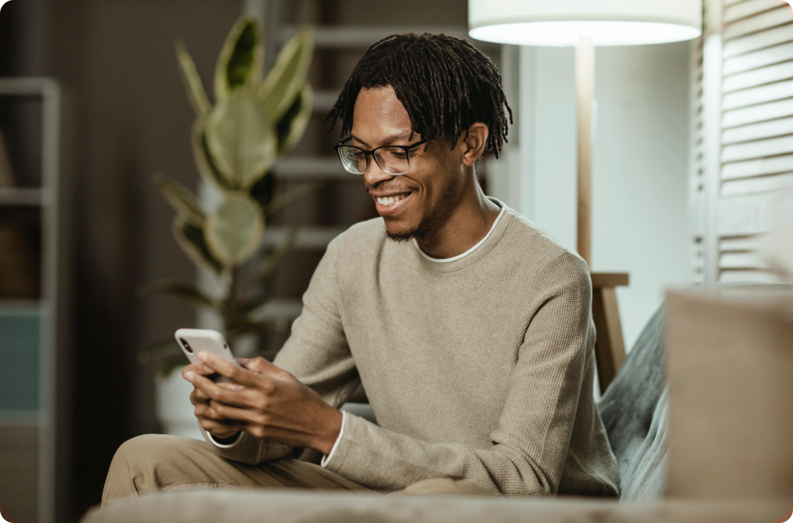 Homem negro com moletom bege usando o celular e sorrindo